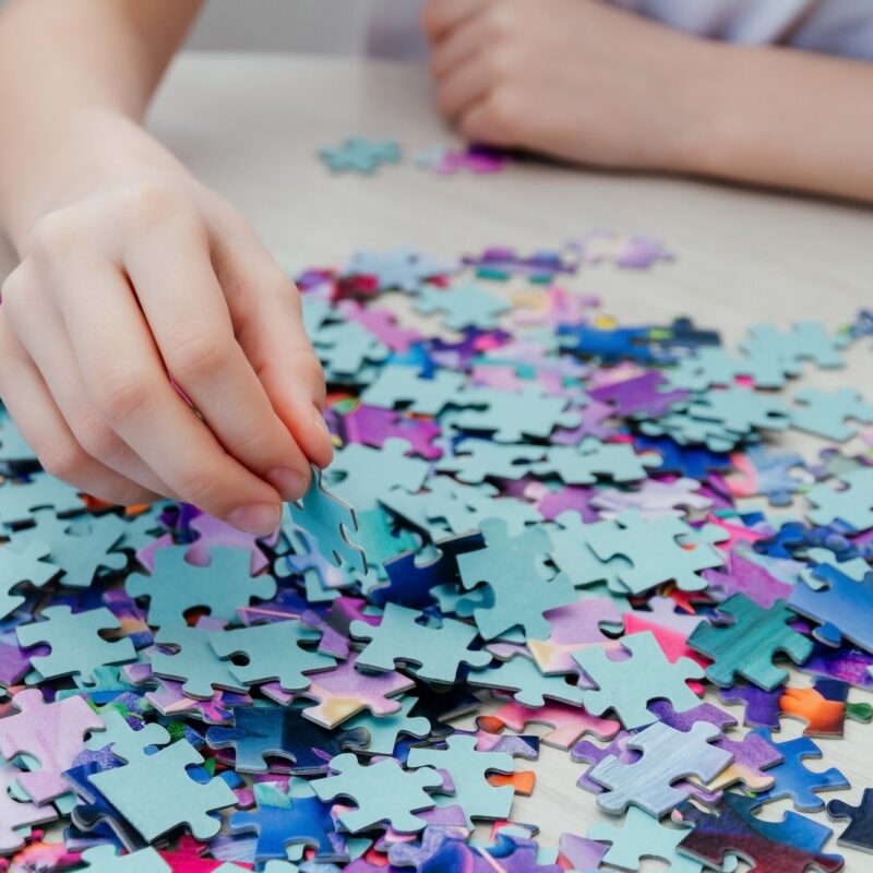 Caucasian girl collects puzzles on the table.